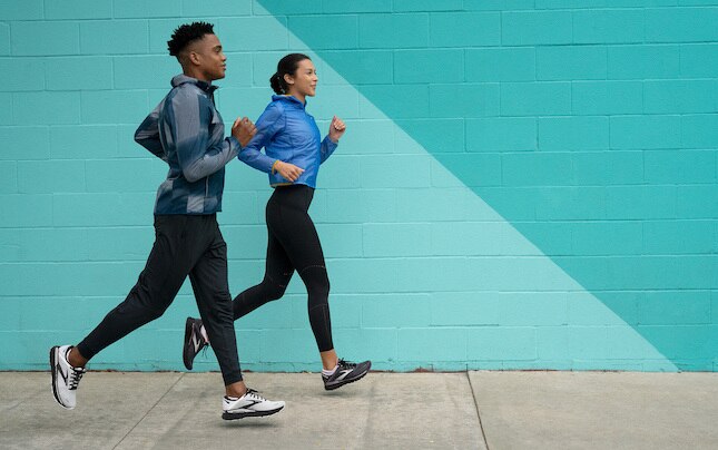 Two runners jog alongside a painted wall