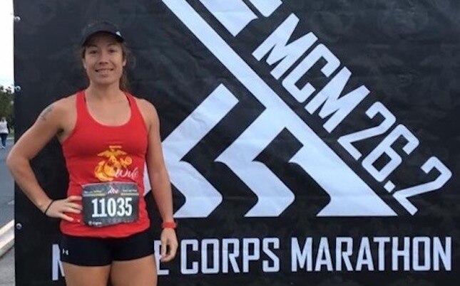 Marathon runner standing in front of a Marine Corps Marathon sign