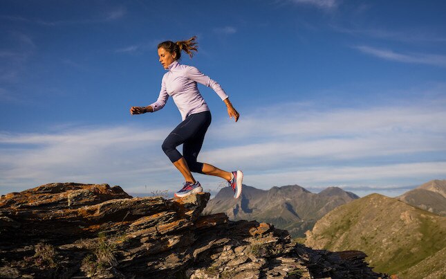A runner leaps over rocky terrain on a trail run.