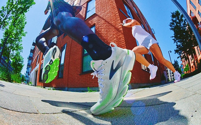 Angled close-up of the Brooks Glycerin Flex, while someone is running on the sidewalk along a city street corner.