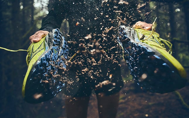 someone smacking together a pair of Cascadia 19 trail running shoes with dirt flying off the shoes