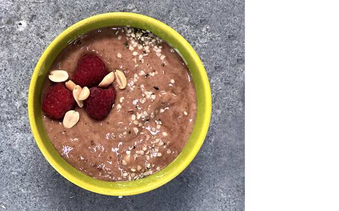A top-down photos of choco-chia mousse topped with fresh raspberries, peanuts, and maple syrup.
