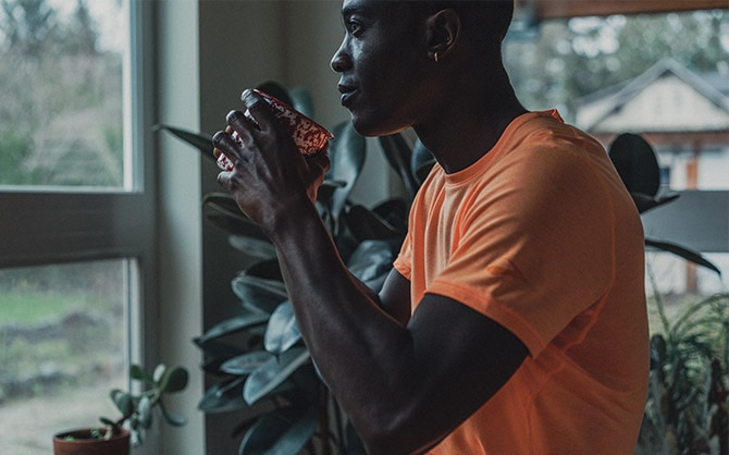 Un runner à l’intérieur, une tasse à la main, observant le froid du dehors