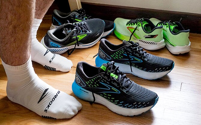 Three pairs of Brooks shoes on a hardwood floor