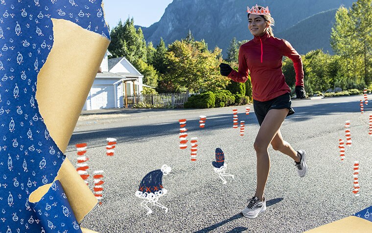 A runner wearing a read long sleeve half zip and shorts runs on a road with mountains in the background.