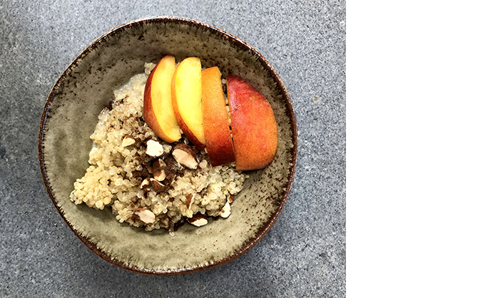 Een top-down foto van de perzikachtige quinoa-ontbijtkom met gesneden amandelen, stukjes verse perzik en bruine suiker.