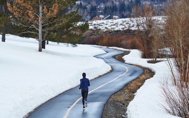 Runner going down a paved trail with snow