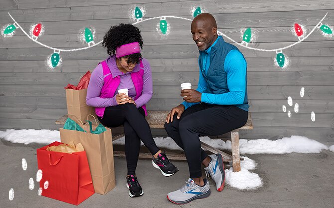 Two people sitting on a bench drinking coffee surrounded by holiday gifts