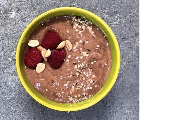 A top-down photos of choco-chia mousse topped with fresh raspberries, peanuts, and maple syrup.