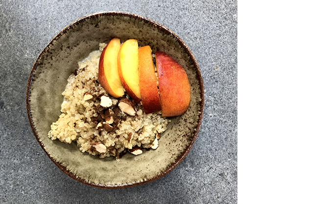 Een top-down foto van de perzikachtige quinoa-ontbijtkom met gesneden amandelen, stukjes verse perzik en bruine suiker.