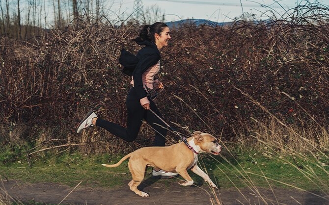 Donna corre con il suo cane al guinzaglio in un sentiero di campagna