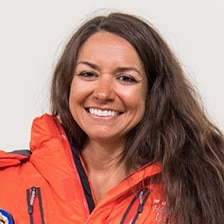 Een profielfoto van de auteur, Roxanne Vogel, die op grote schaal glimlacht in een feloranje jas.