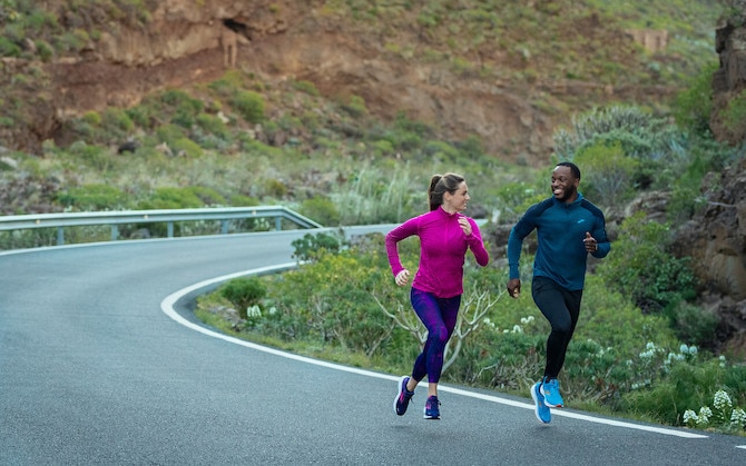 Two people running down a windy road.