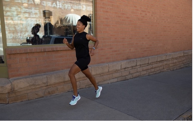 Woman running on sidewalk next to brick building