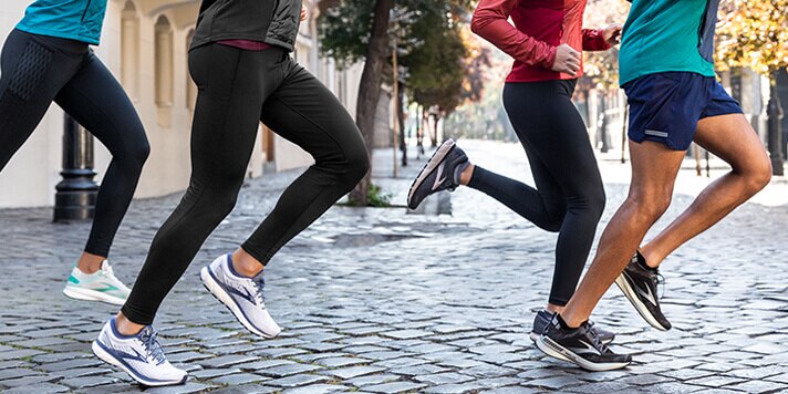 Four individuals run together as a group across a cobble-stone square.