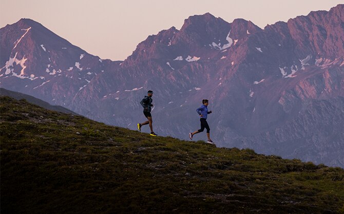 Due runner corrono in montagna con cime sullo sfondo