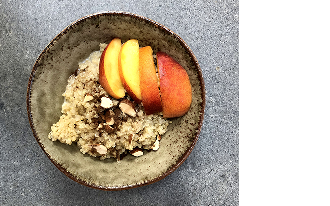 A top-down photo of the peachy quinoa breakfast bowl topped with sliced almonds, pieces of fresh peach, and brown sugar.