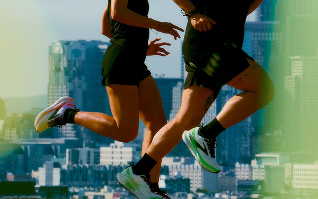 Twee mensen lopen op de Brooks Glycerin 23 met een stadsgezicht op de achtergrond
