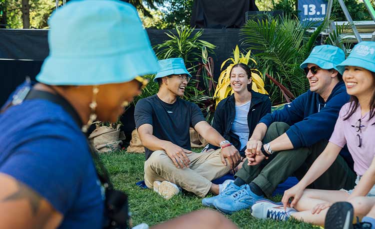 A group of people wearing hats, smiling and sitting on a lawn