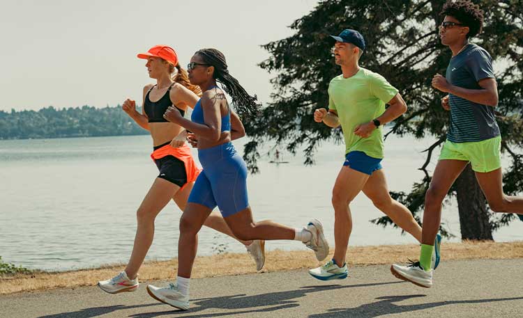 A group of people in colourful clothing run past a body of water.