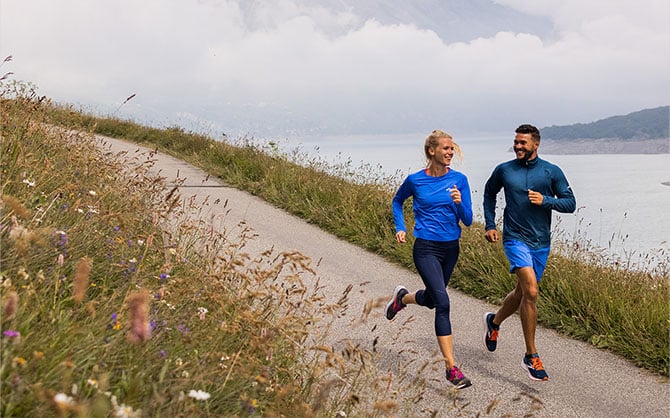 Two runners on a path surrounded by meadows and a river