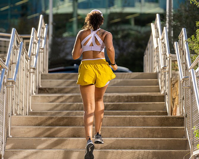 Une photo d’une femme portant une brassière de running Drive Mesh jaune courant près d’un champ.
