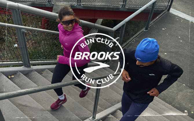 Two people run up a staircase, behind a Brooks Run Club logo