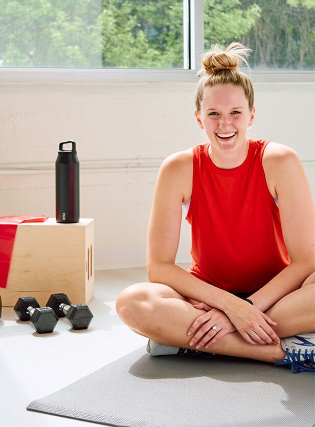 Woman sitting on the floor next to dumbbells.