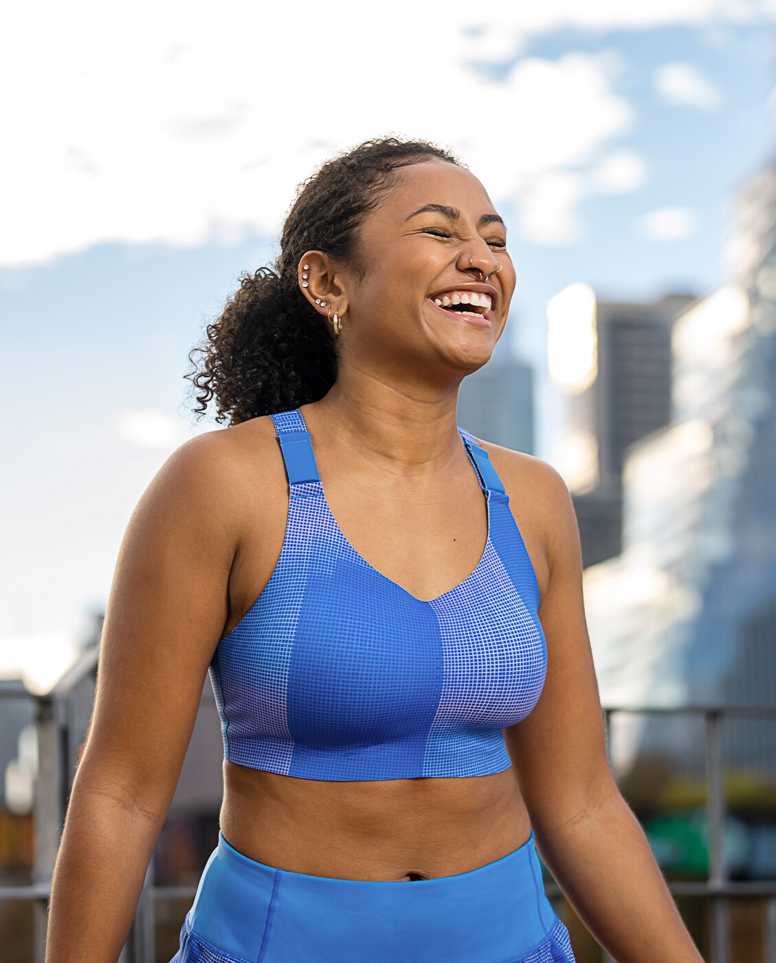 A woman smiling on the street, one in a blue Brooks Run Bra