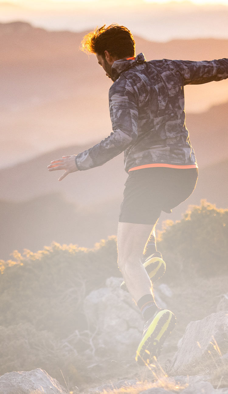 Model with Brooks outerwear running down a rocky hill