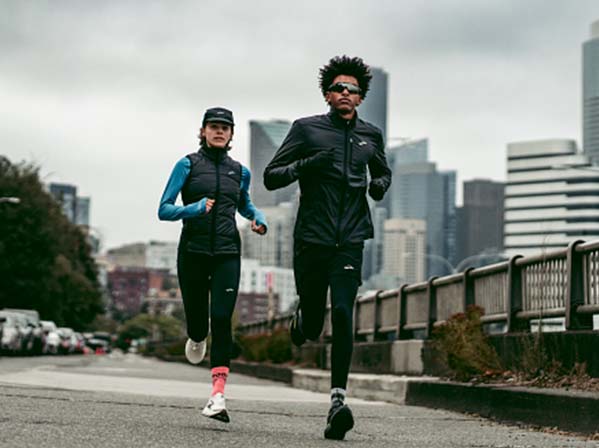 Two people run outside on a city sidewalk