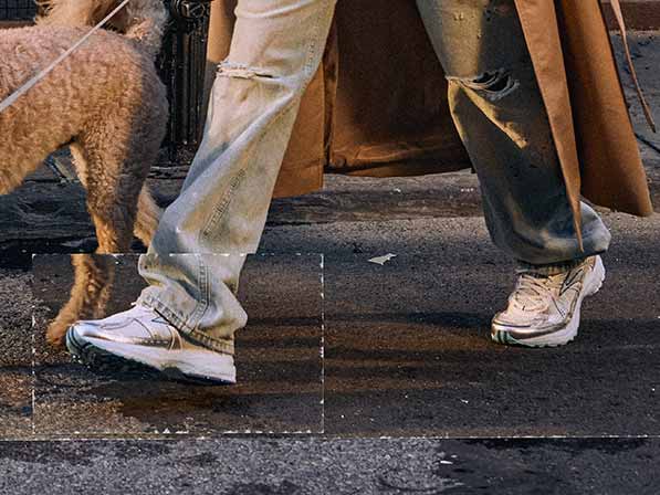 A person wearing Brooks shoes and blue jeans walks a dog across a sidewalk
