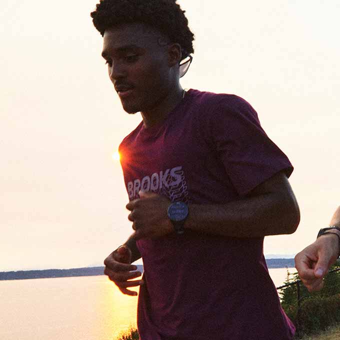 A man wearing the Graphic Short Sleeve runs outside, in front of an orange sunset