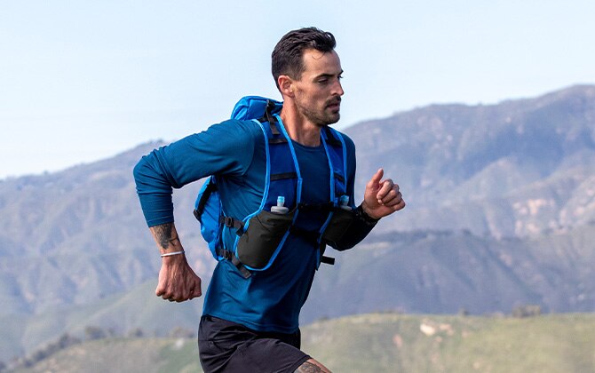 A man running on a trail with a backpack and mountains in the background