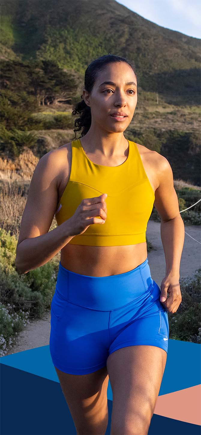 A woman wearing a yellow Drive 3 pocket run bra running in the mountains.
