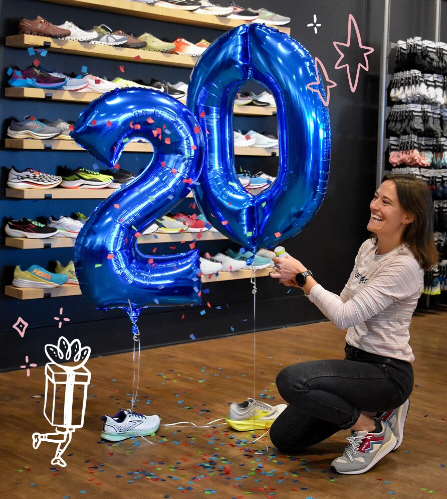 Woman posing with two balloons that say "20" and are tied to Brooks shoes.