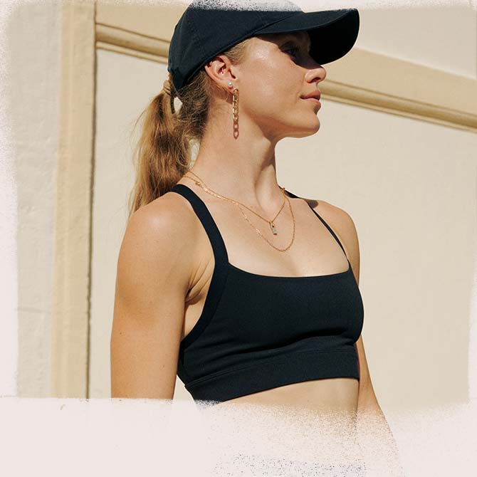 A woman wearing a Brooks sports bra and hat looks to the side