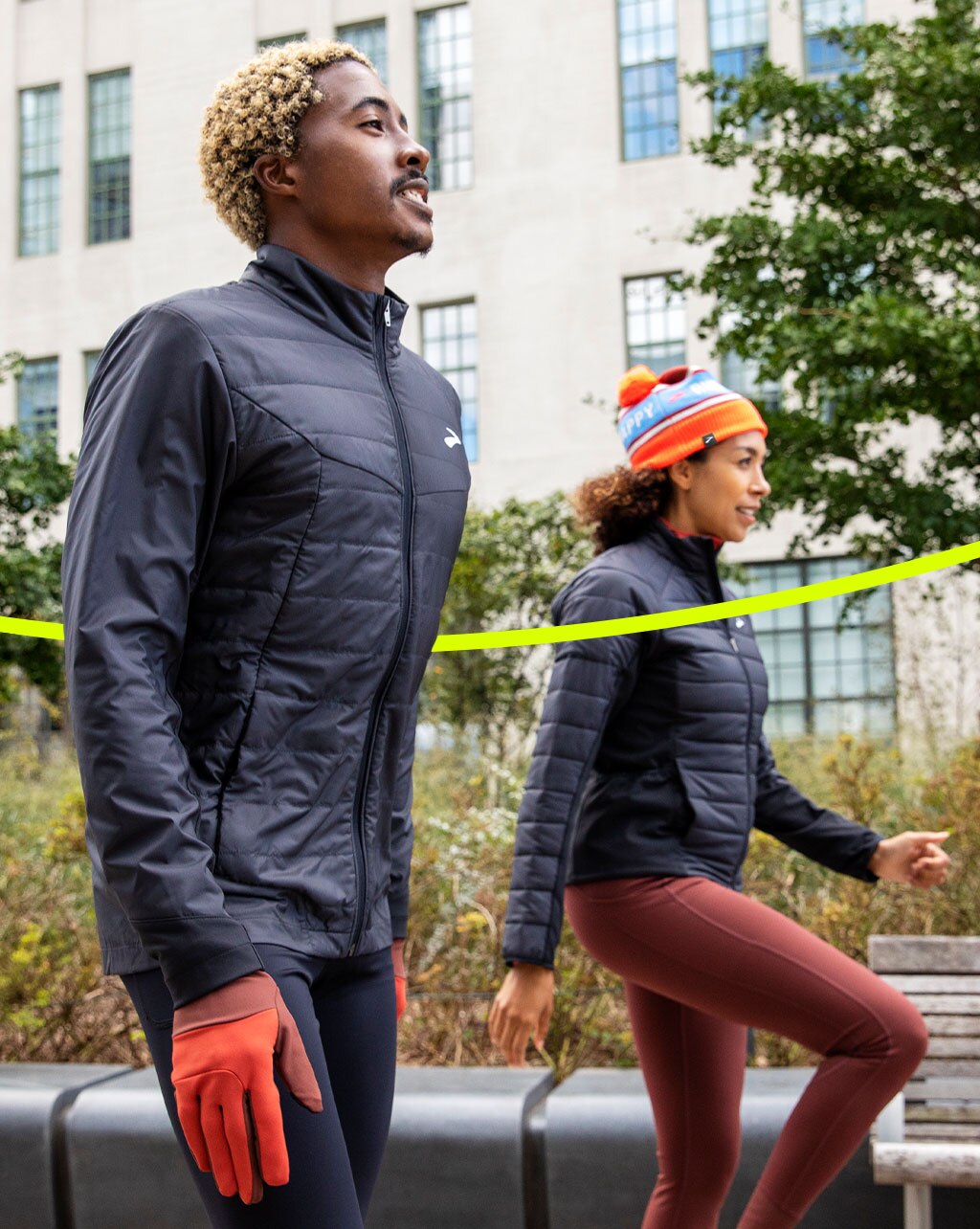 Side view of two people walking next to building wearing Brooks black jackets