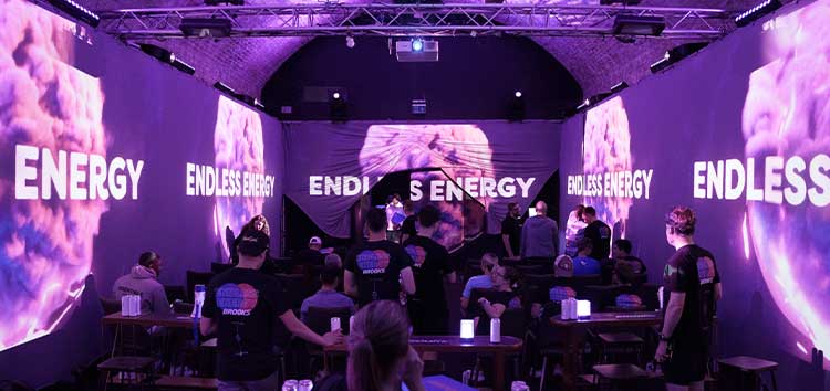 Des personnes se tenant debout dans une pièce violette avec des murs où l’on peut lire « Une énergie sans fin »