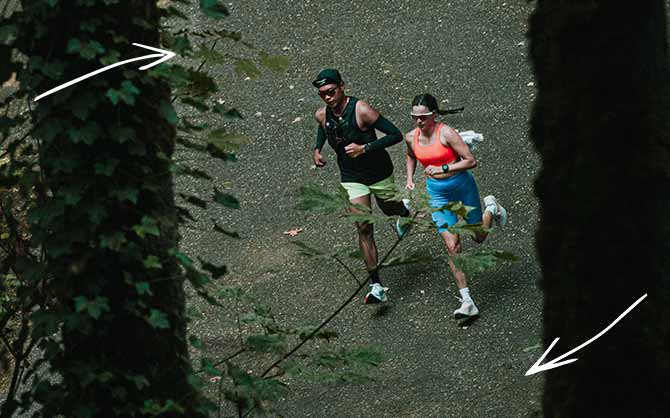 Two people in bright gear running in a dark, natural setting