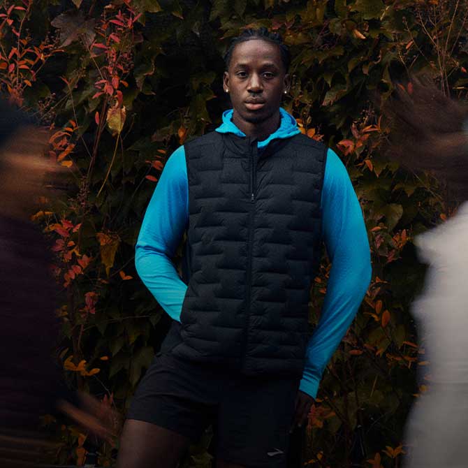 Un homme portant des vêtements Brooks regardant droit devant lui, debout devant un paysage naturel.
