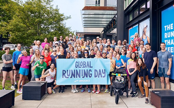 Gruppe von Brooks-Mitarbeiter*innen mit einem Schild mit der Aufschrift „Global Running Day“