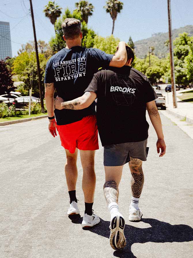 Two people in Brooks gear walk side by side down a sunny street