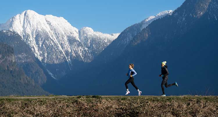 Two people run next to snowy mountains.