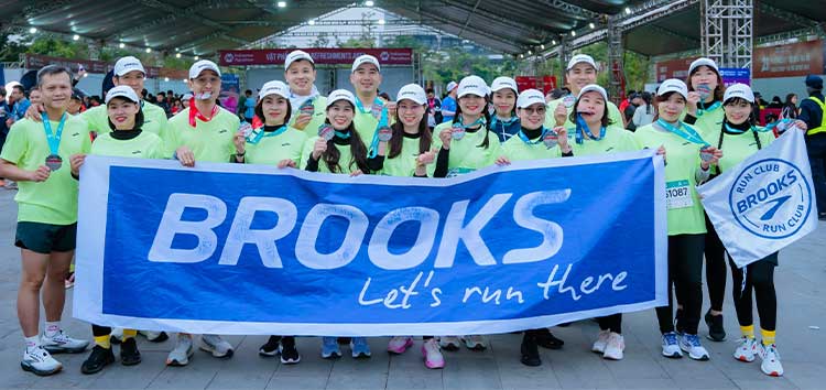 A group of people stand behind a Brooks banner