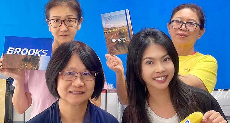 Four people smile while holding Brooks notebooks
