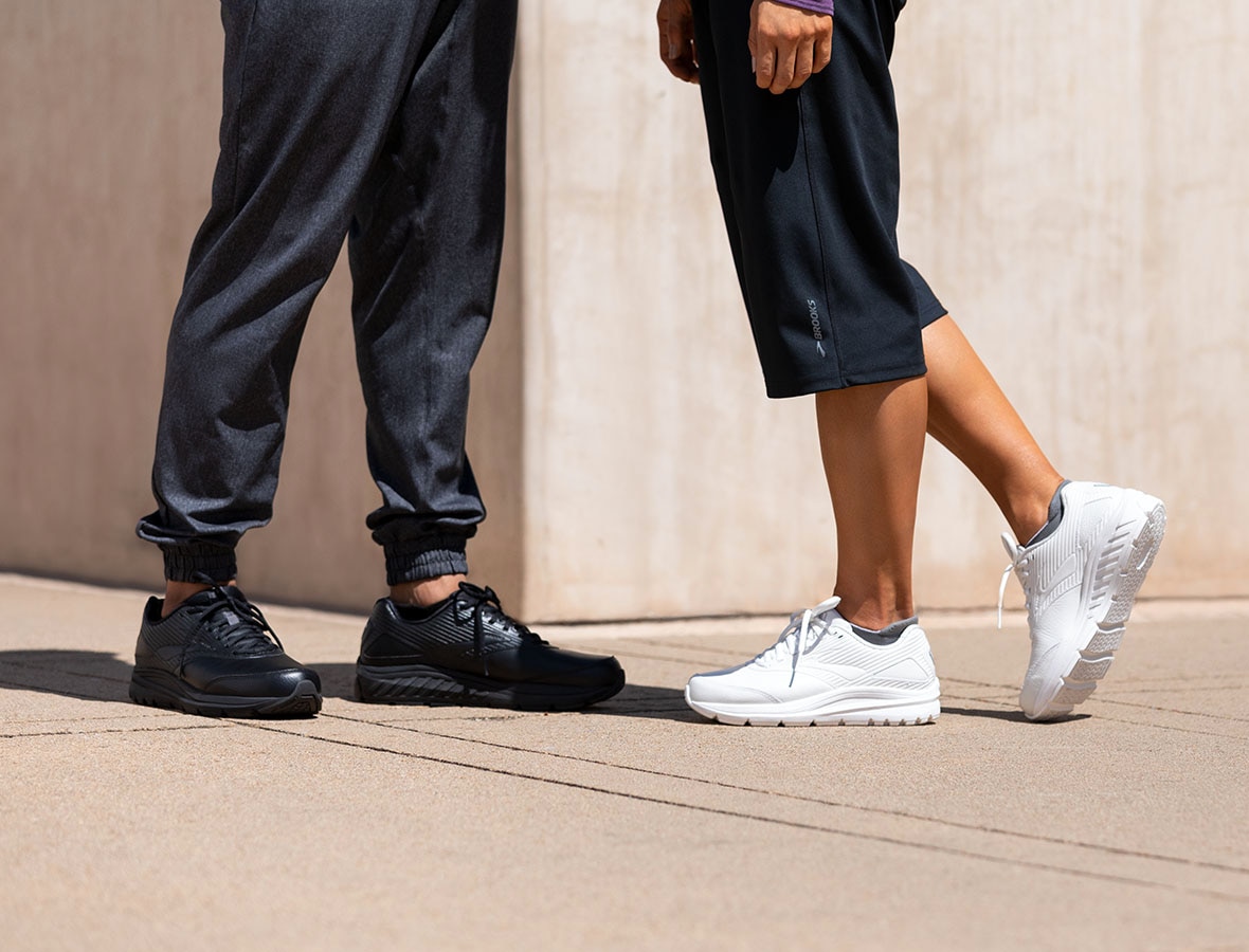 A picture of two people from the waist down; they are both wearing the Addiction Walker 2, one in black and one in white