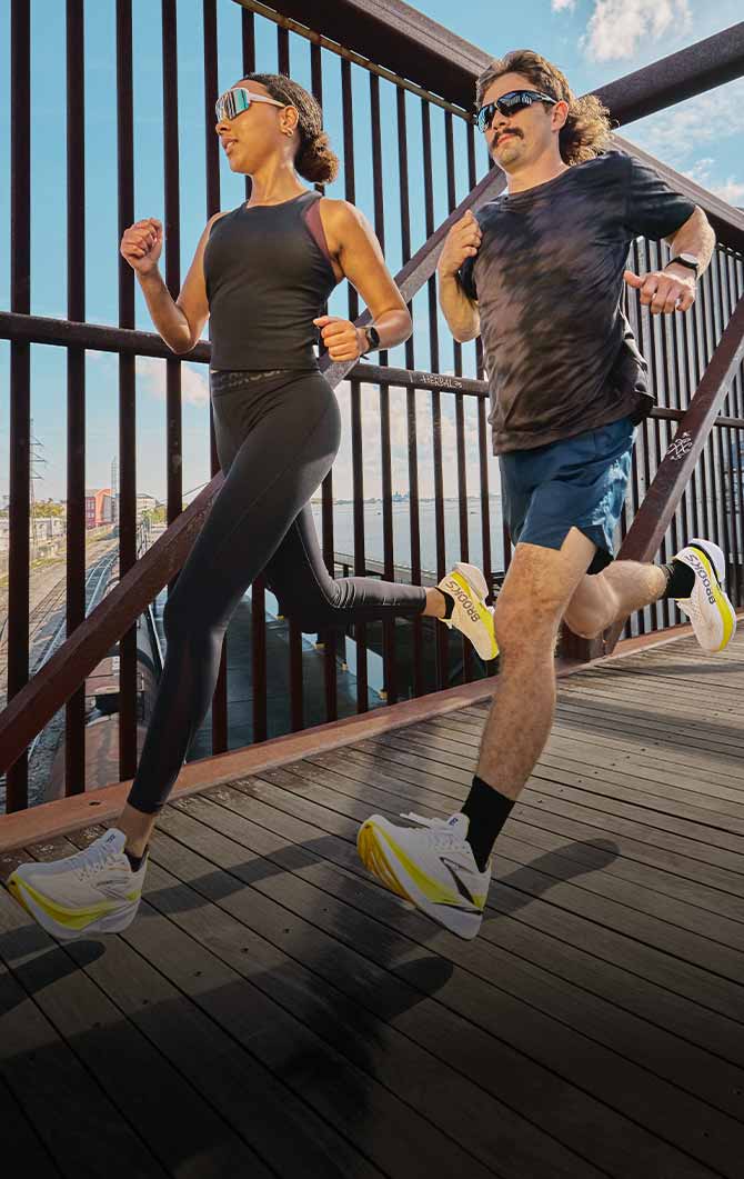 Two people run side-by-side down a bridge on a sunny day