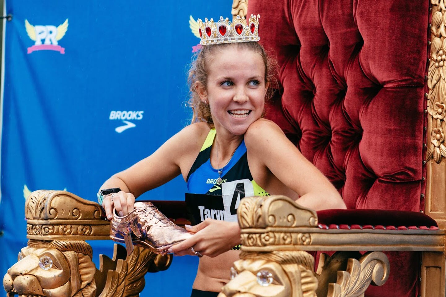 An athlete sits on a throne with a crown and holding a golden shoe