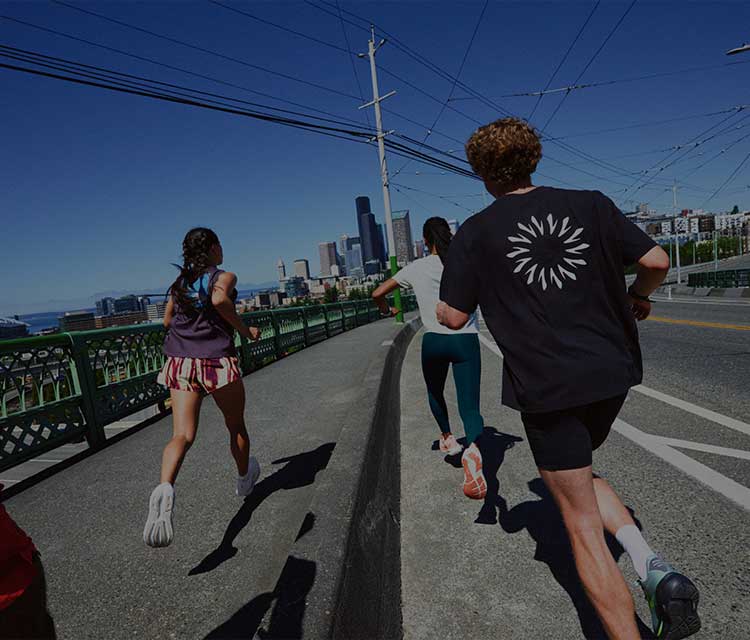 A group of people wearing Brooks gear run down a sidewalk on a sunny day
